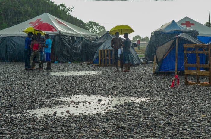 African migrants stand under umbrellas in a camp.