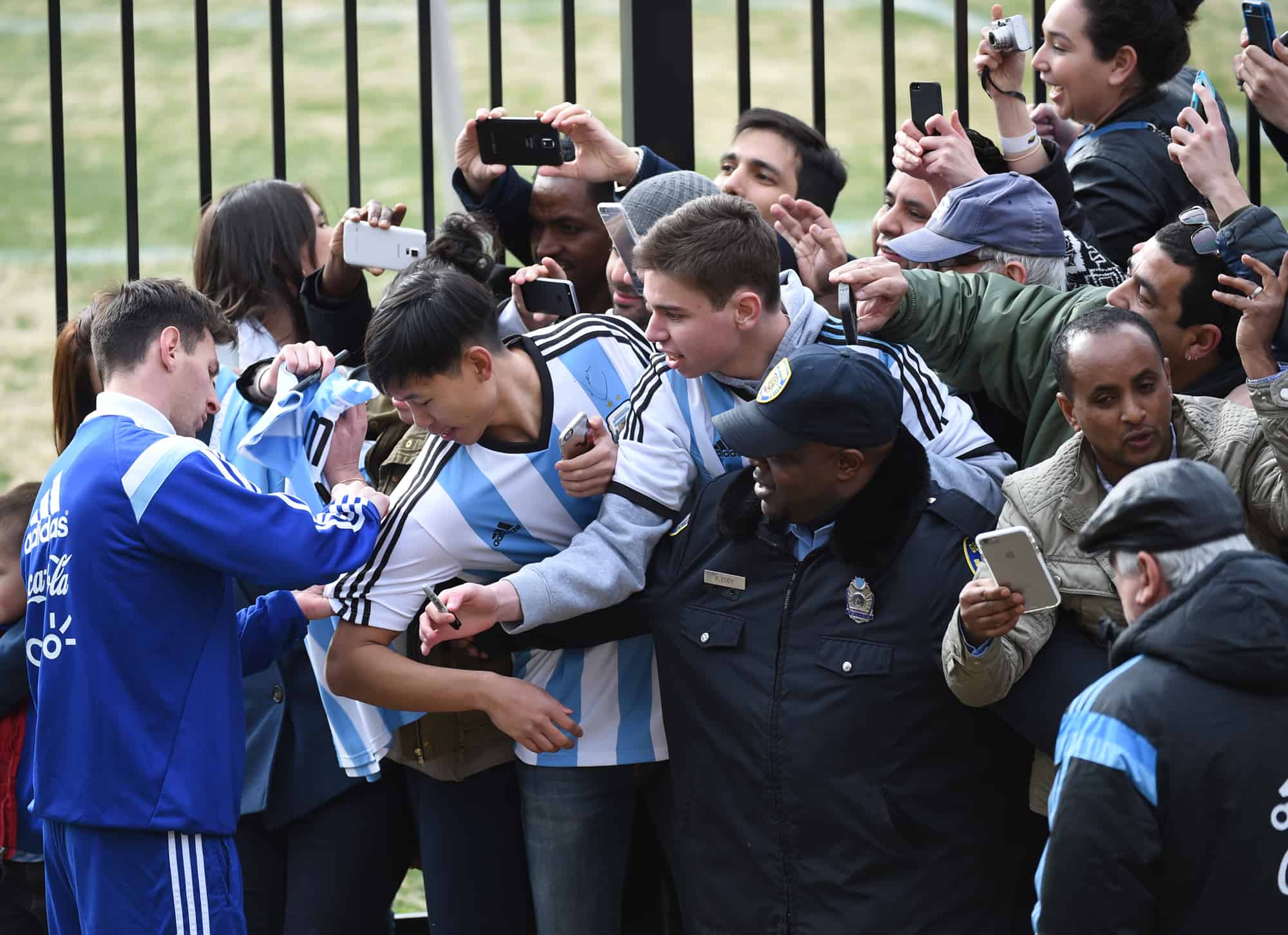 Lionel Messi, left, signs autographs for some of the hundreds of fans who showed up for a glimpse of the Argentine national team's practice at Georgetown University in Washington, March 24, 2015.