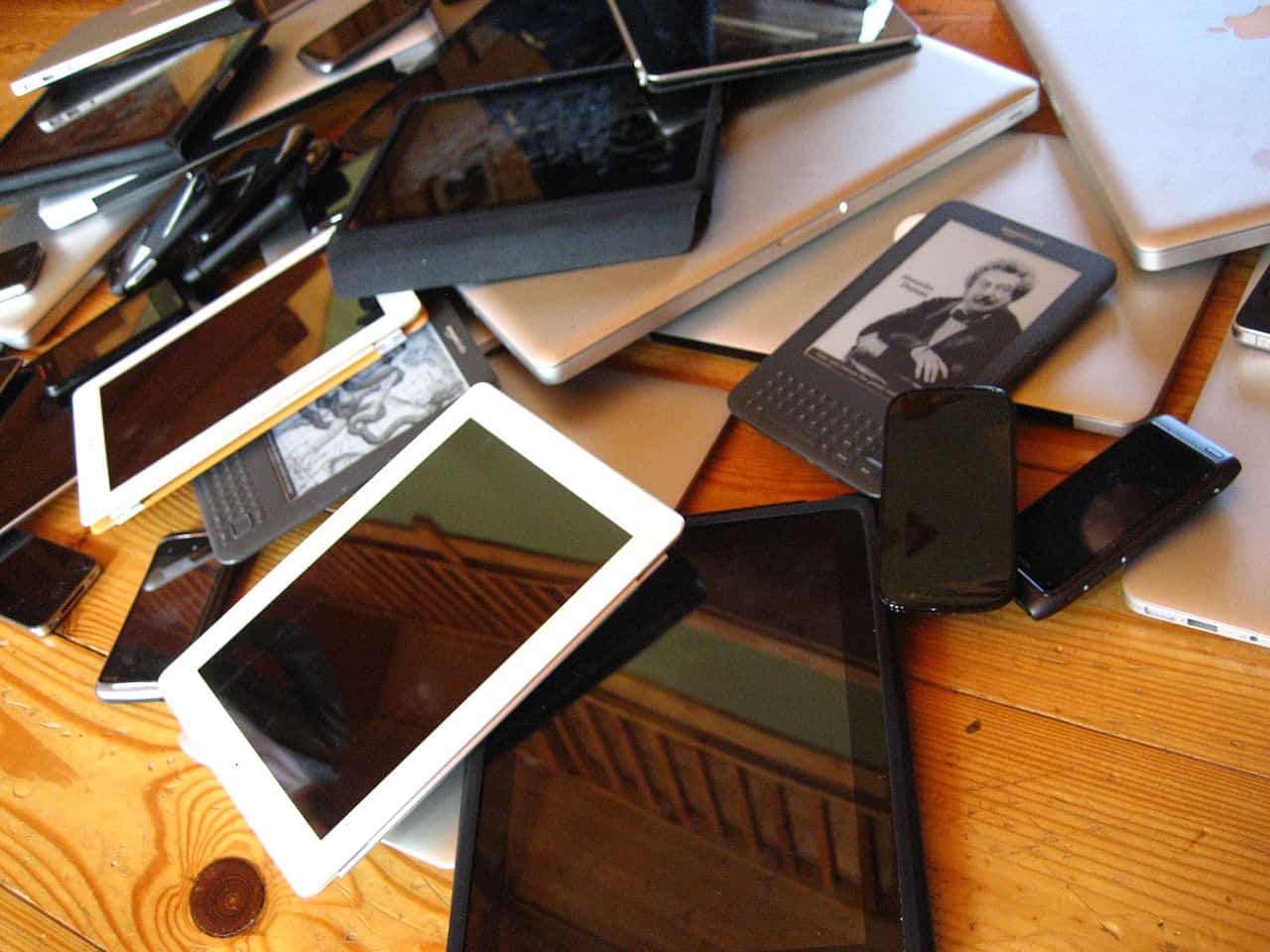 A pile of mobile devices including smart phones, tablets, laptops and ebook readers.