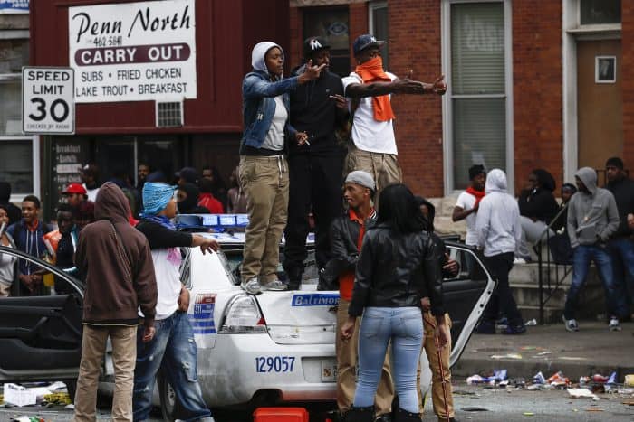 People stand on a damaged Baltimore Police car.