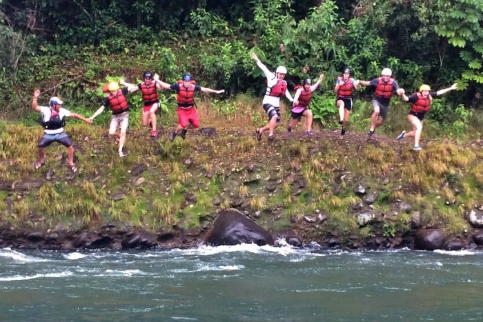 A bunch of rafters jump off a cliff into a river.