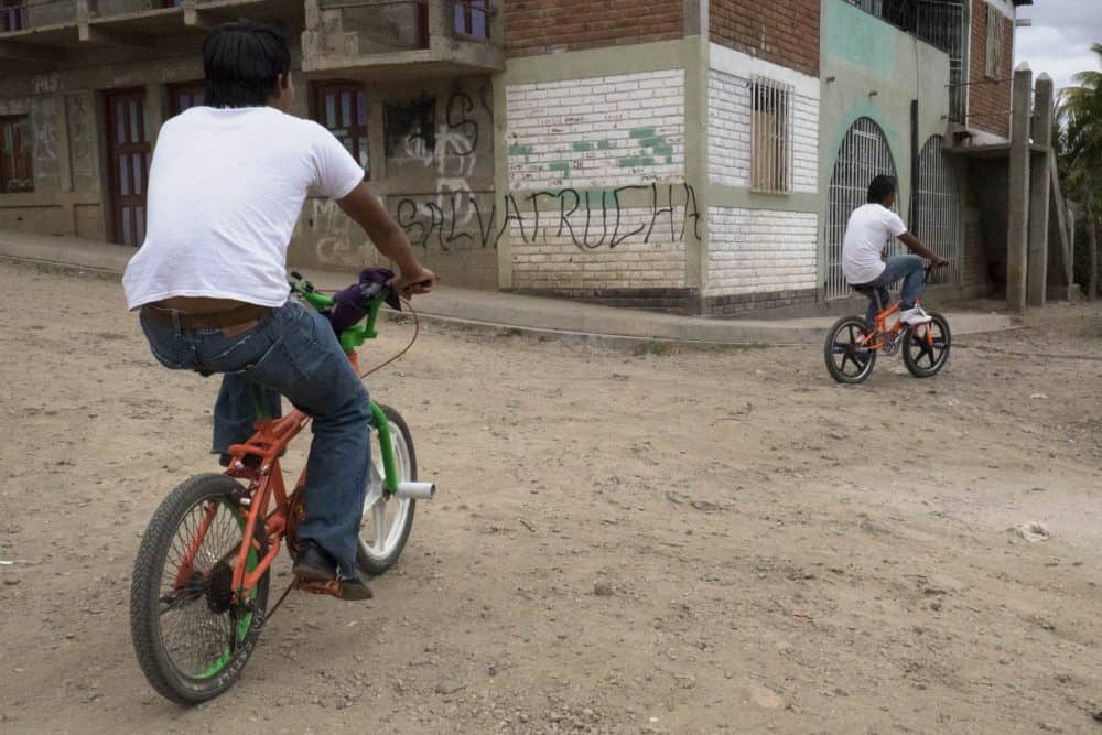 Boys bike past gang graffiti on a wall in Somoto.