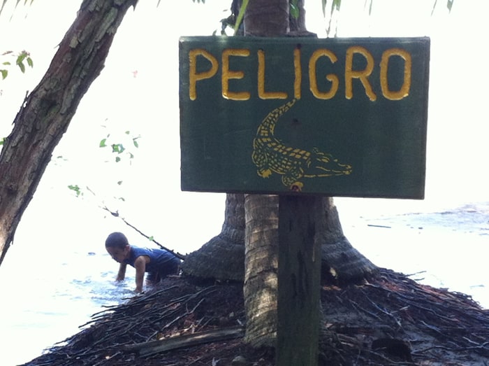 A child plays in the shallows behind a sign warning of crocodiles.