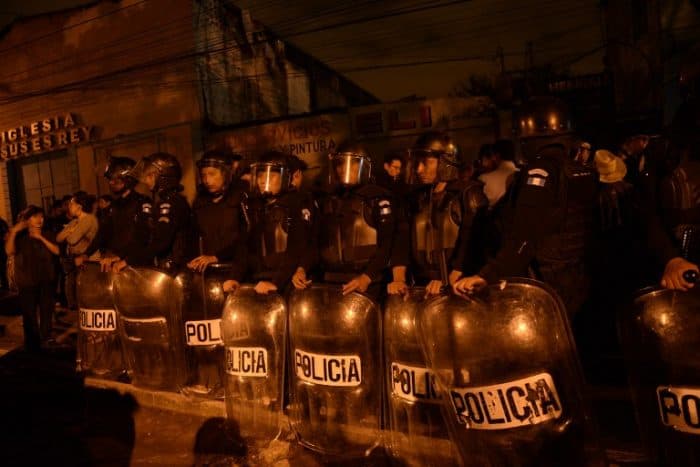 Riot police stand guard as indigenous people protest for the release of other protesters being held inside a bus by the National Civil Police after they participated in demonstrations to demand the resignation of Guatemalan President Otto Perez Molina as a corruption scandal rocks the government, in Guatemala City late on June 13, 2015.