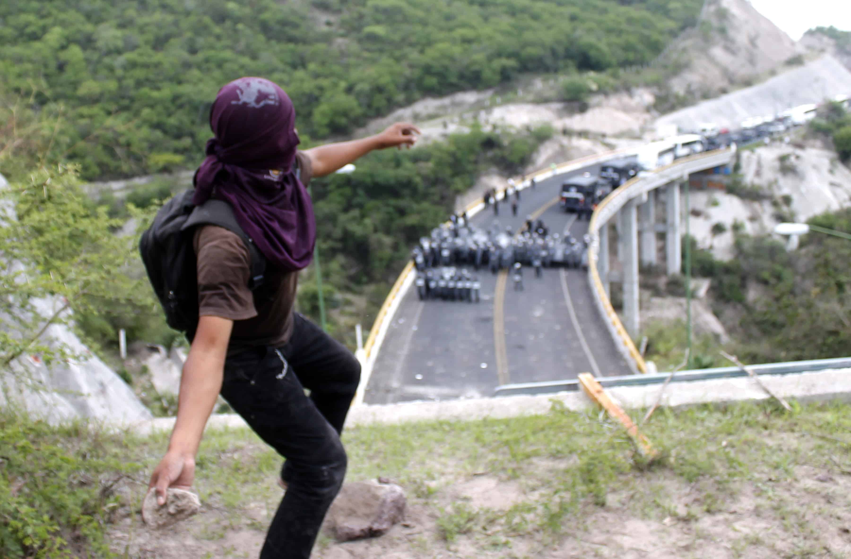A protester from Ayotzinapa throws stones at the Mexican Federal Police blocking the Chilpancingo-Tixtla highway.