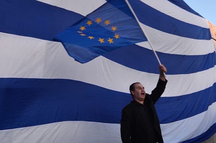 A man waves a European flag in front of a giant Greek one.