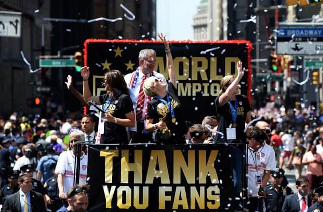 U.S. women's soccer team midfielder Megan Rapinoe (center) holds up the World Cup 2015 trophy as midfielder Carli Lloyd (left), New York City Mayor Bill de Blasio and head coach Jill Ellis (right) wave to the crowd during the ticker tape parade in New York on July 10, 2015.