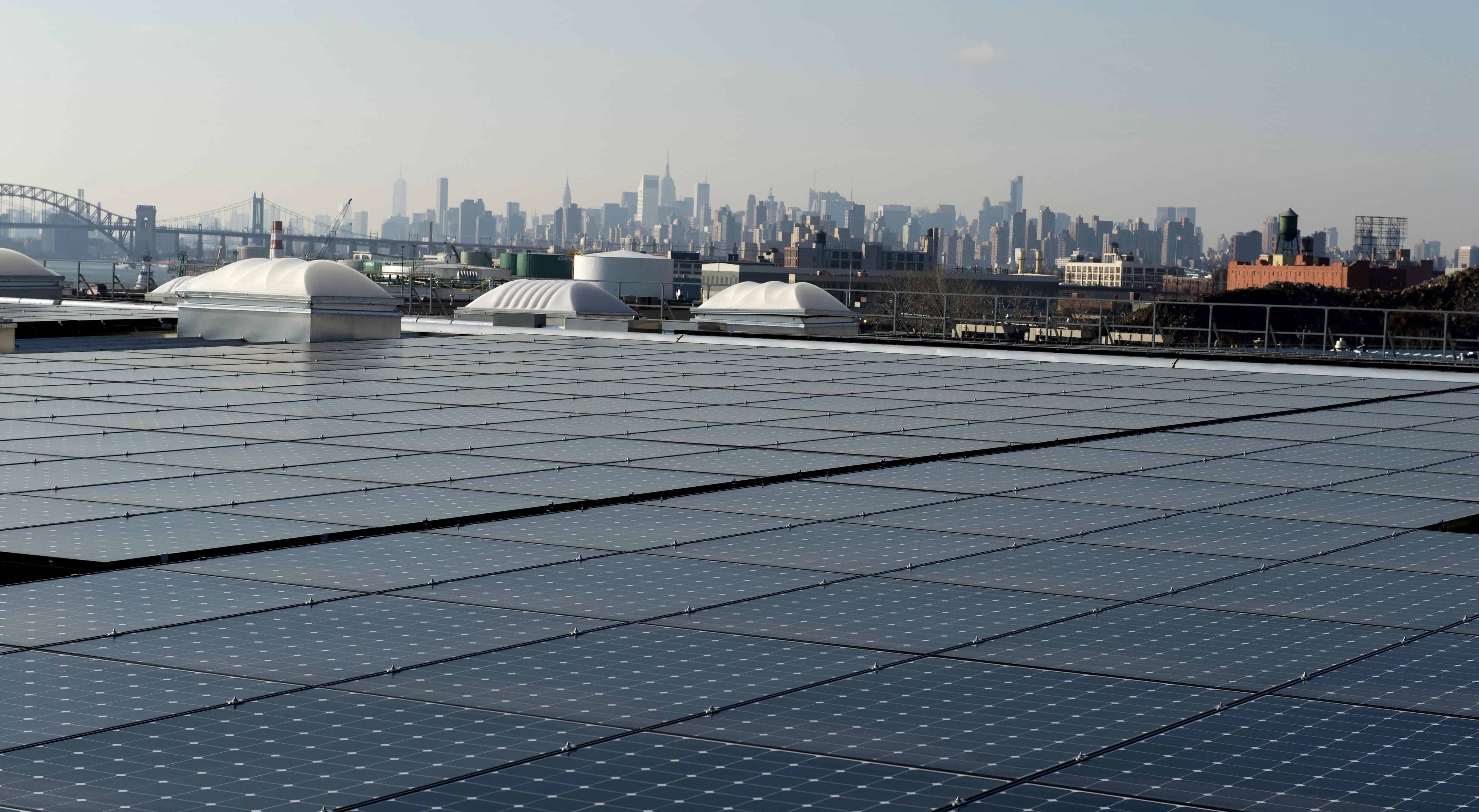 The rooftop of Jetro Restaurant Depot in the Bronx, with a view of Manhattan in the distance, is covered with solar panels.