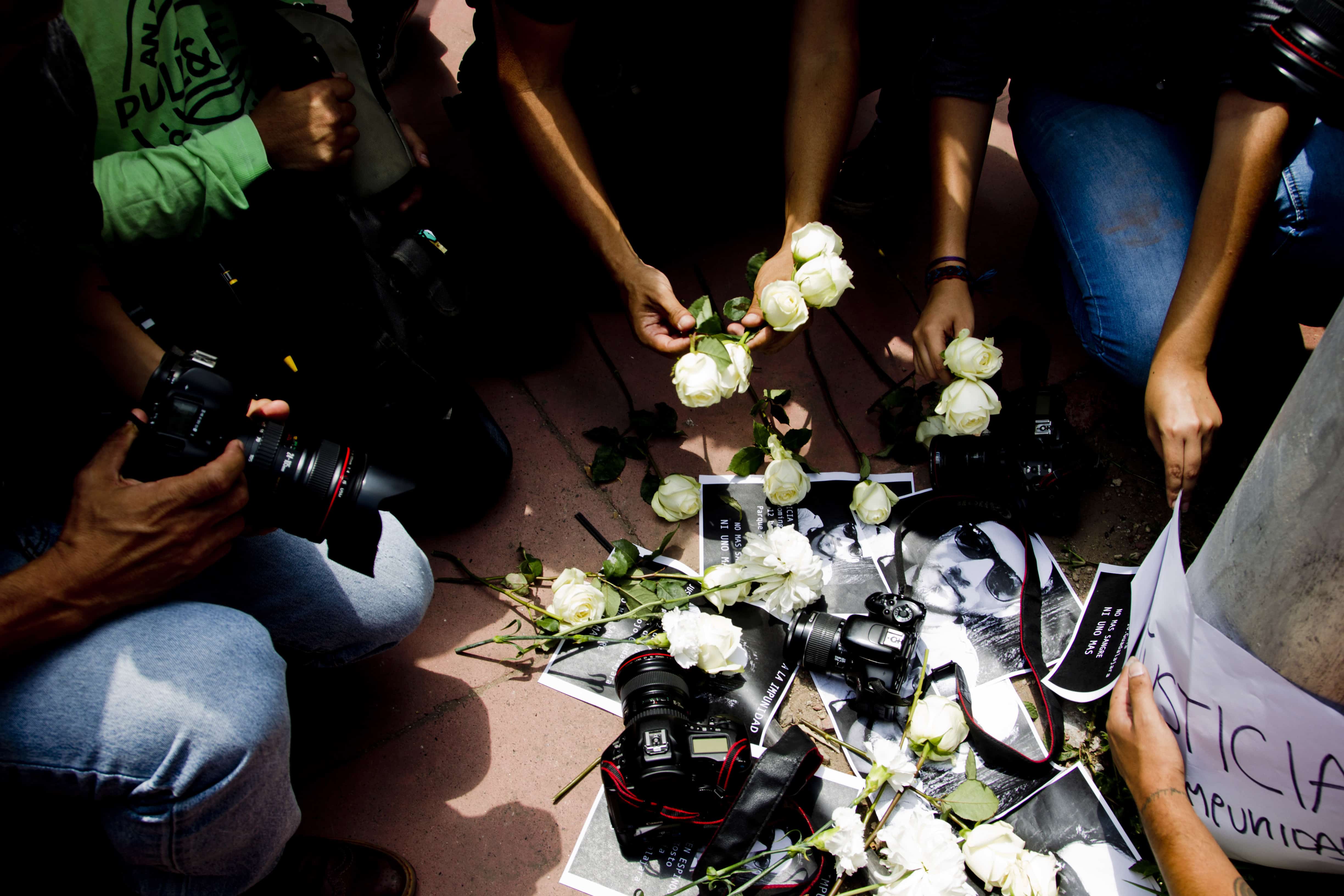 Mexican photojournalists place their cameras on the floor with white flowers .