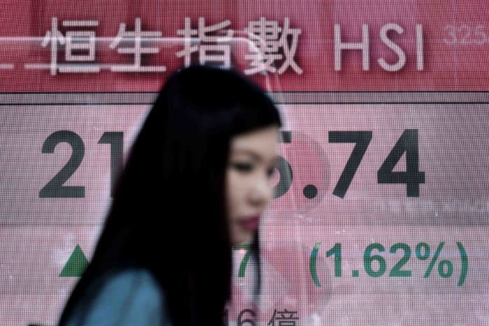 A woman walks past an electronic board displaying financial information in Hong Kong.