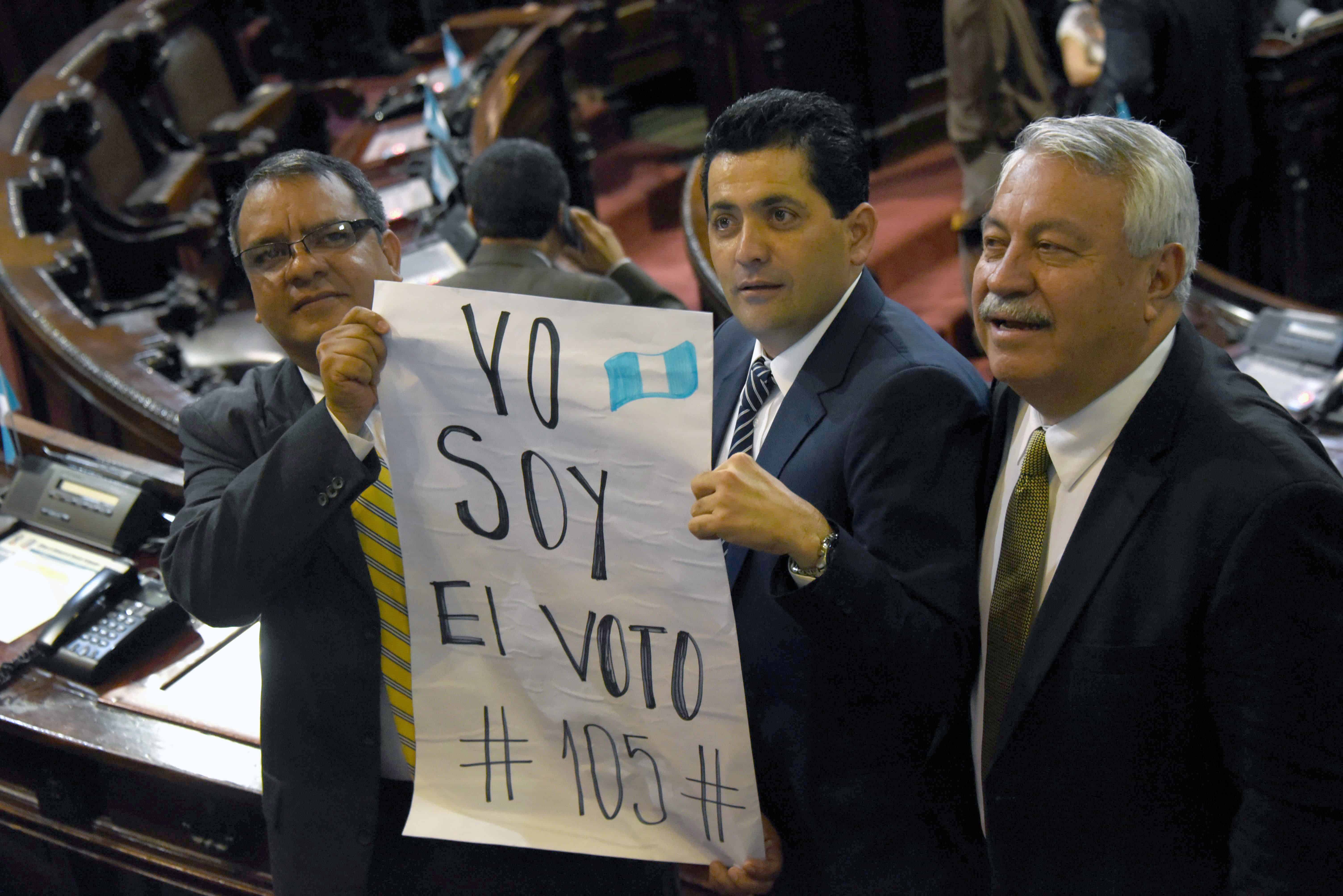 Guatemalan lawmakers Celvin García, left, Óscar Chinchilla, center, and Carlos Fión hold a sign that reads: 