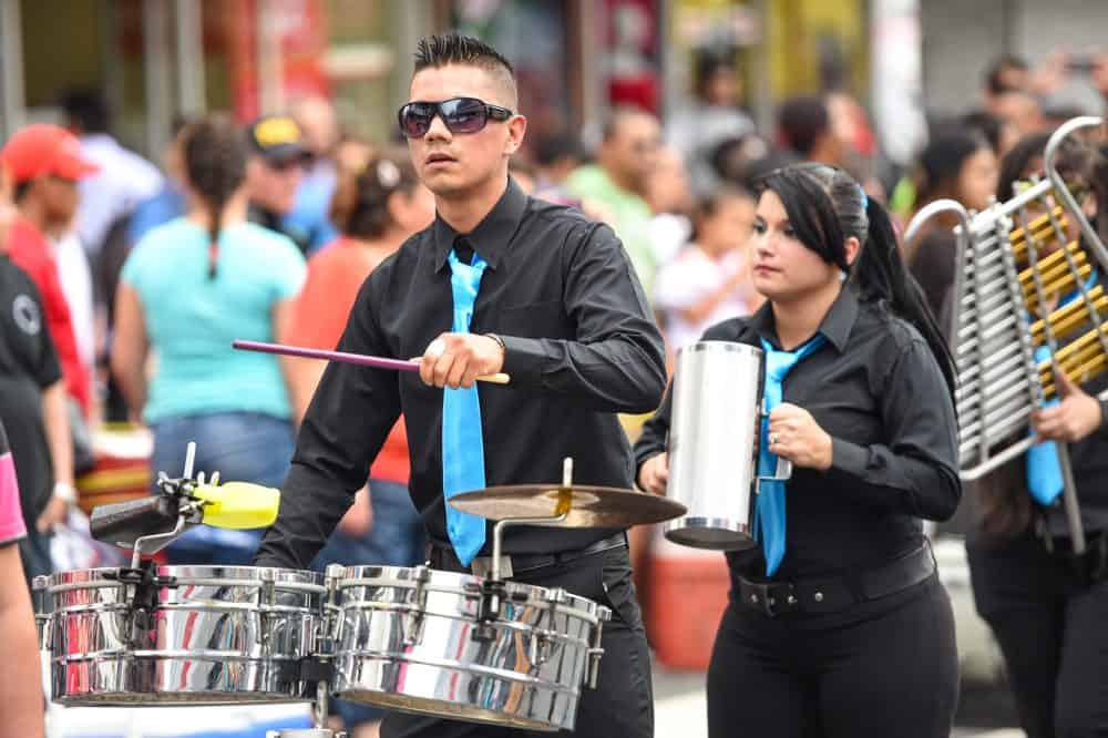 A school band playing music with drums and trumpets during the Independence Day parade along Avenida Segunda.