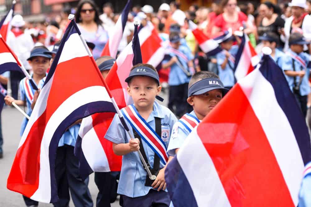 The parade participants waving Costa Rican flags, filling Avenida Segunda with national pride.