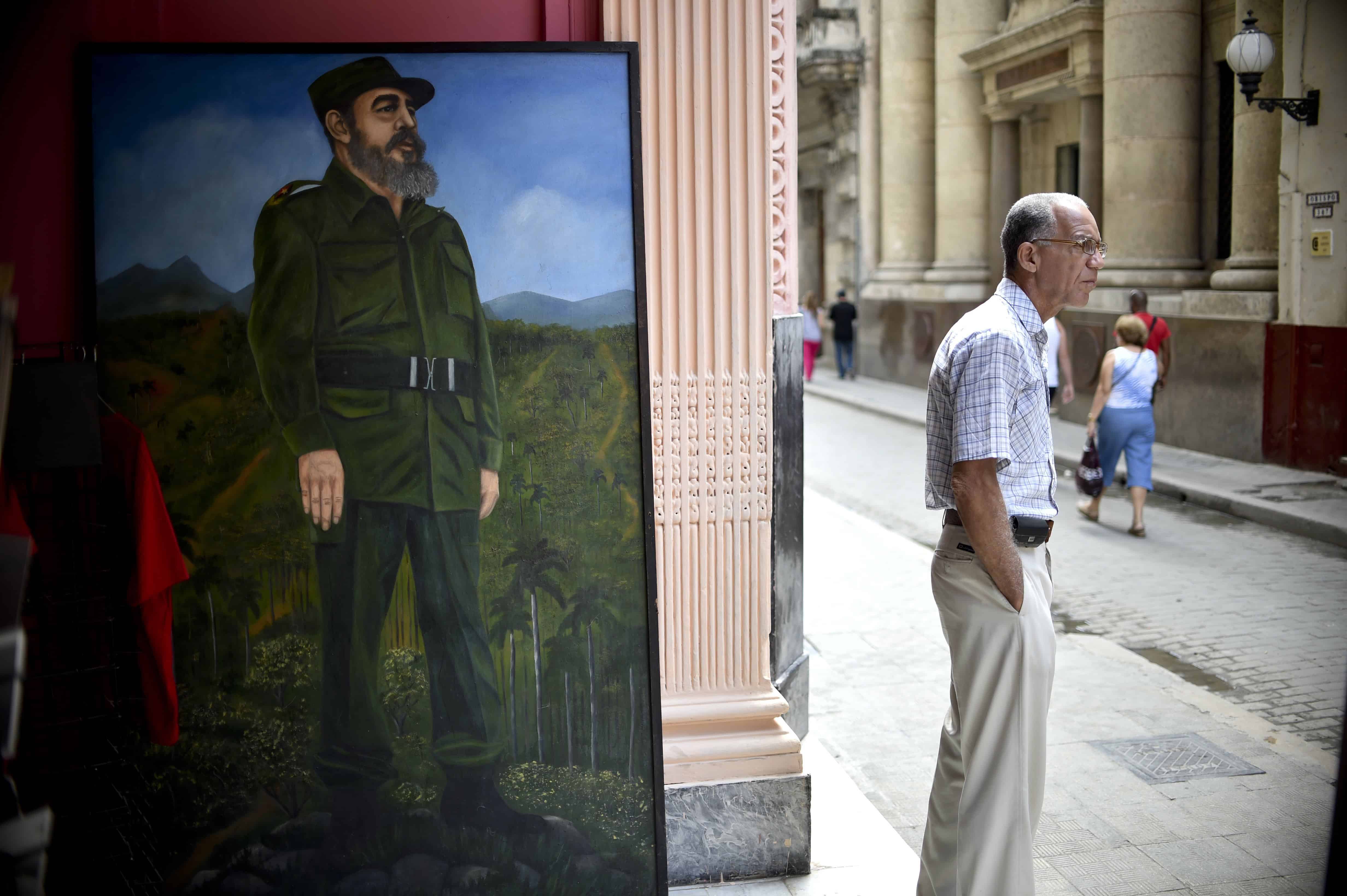 A man stands next to a painting of former Cuban President Fidel Castro