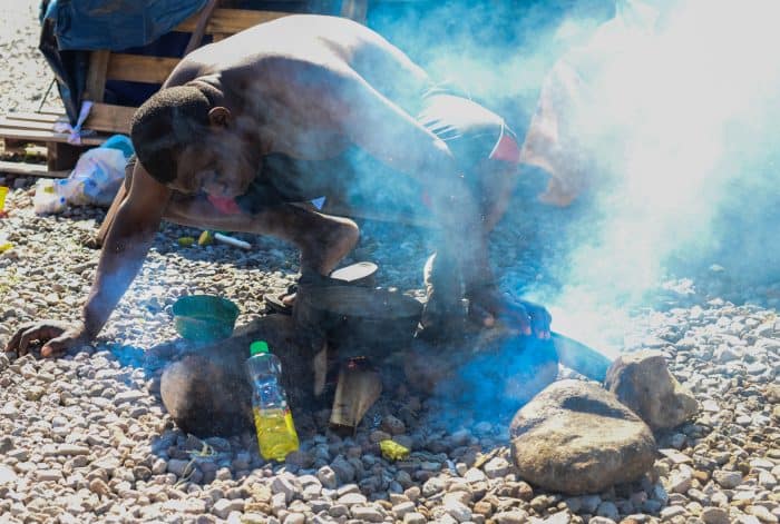 A migrant blows on the flames of a fire