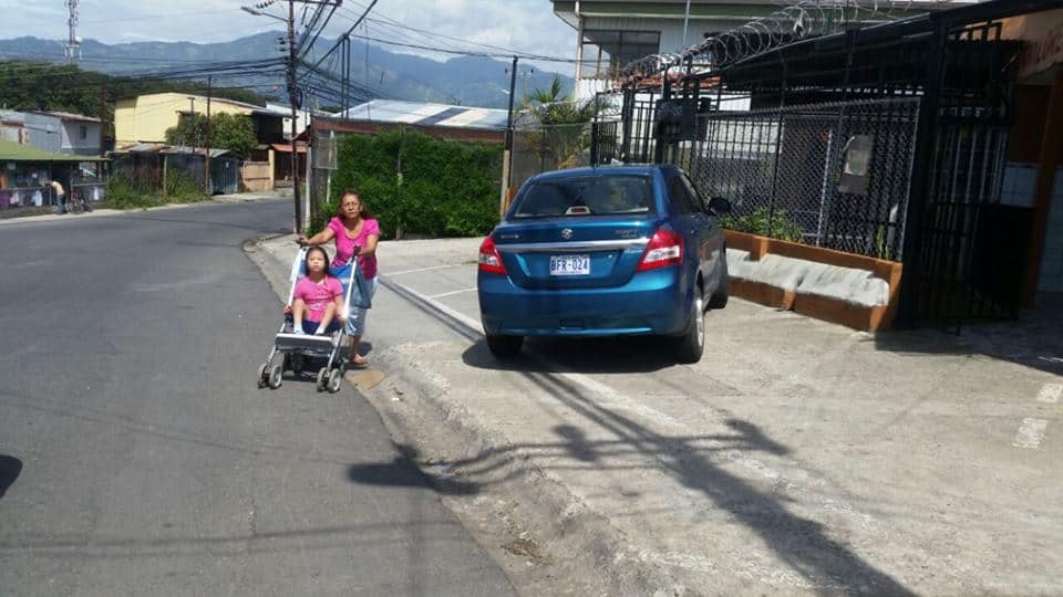 woman with stroller walking in street to get around car parked on sidewalk