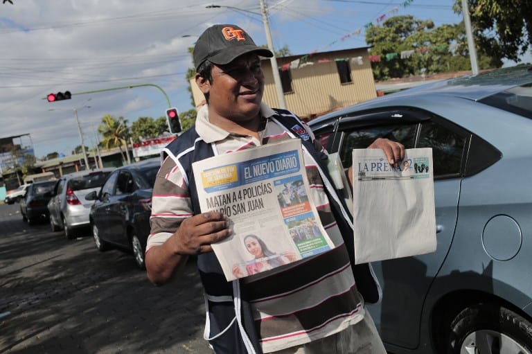 A vendor selling newspapers holds an edition of 